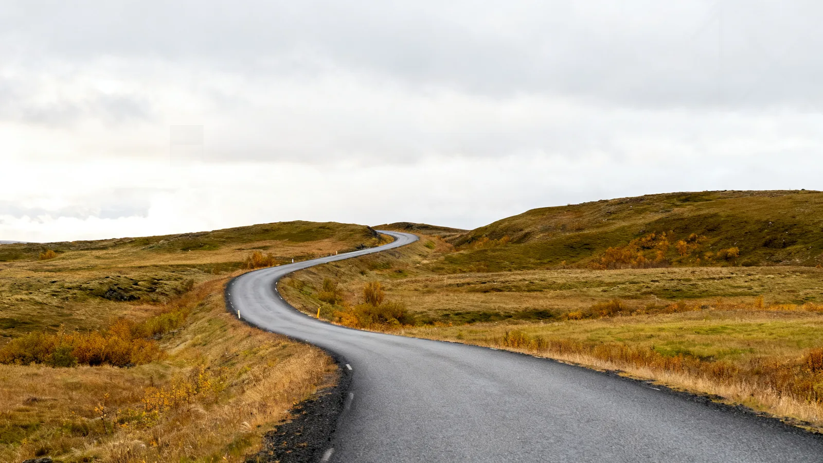 Anonymous rural Icelandic paved road through low grass hills