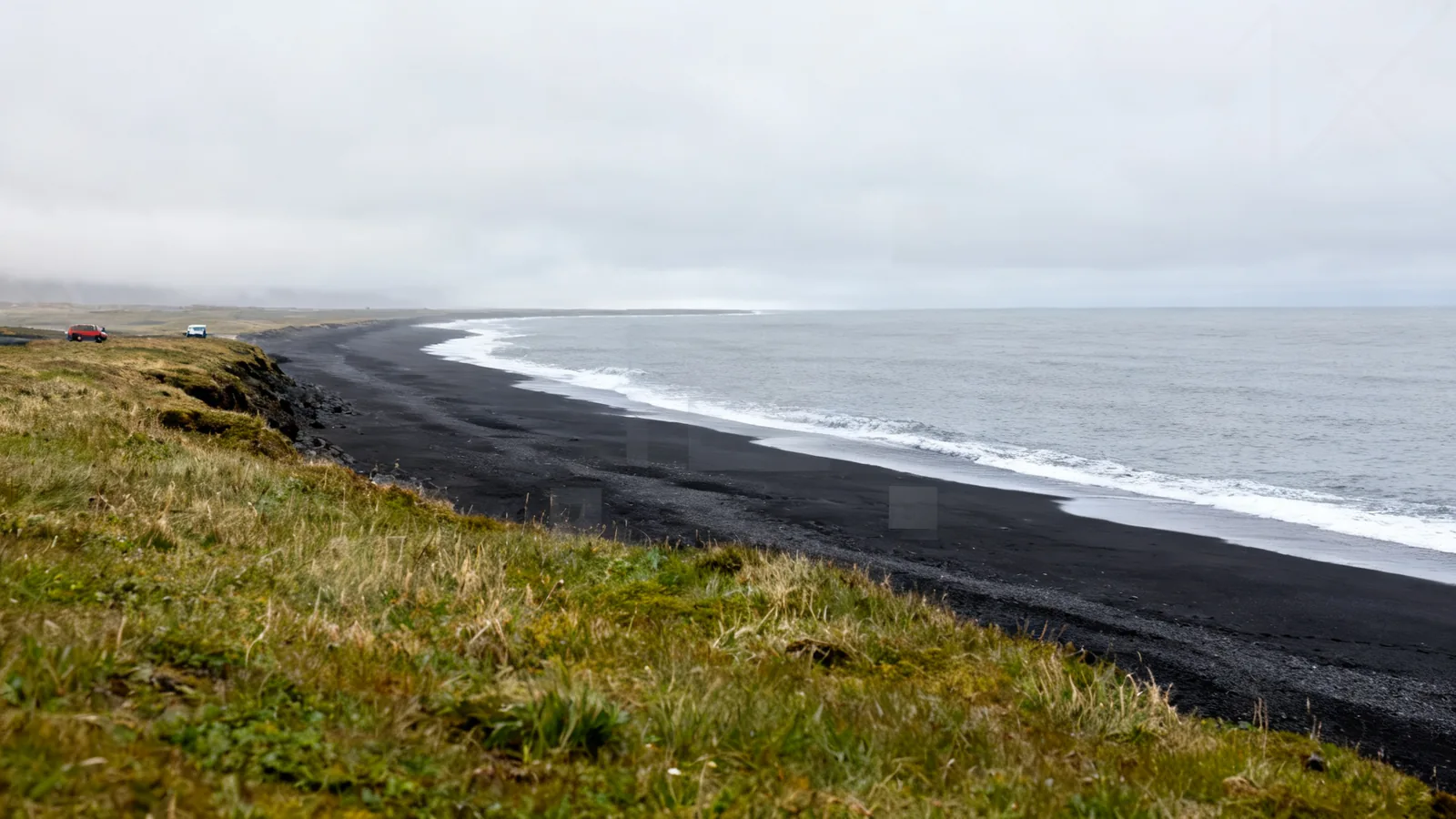 Generic black-sand shoreline and grey ocean viewed from a grassy bank