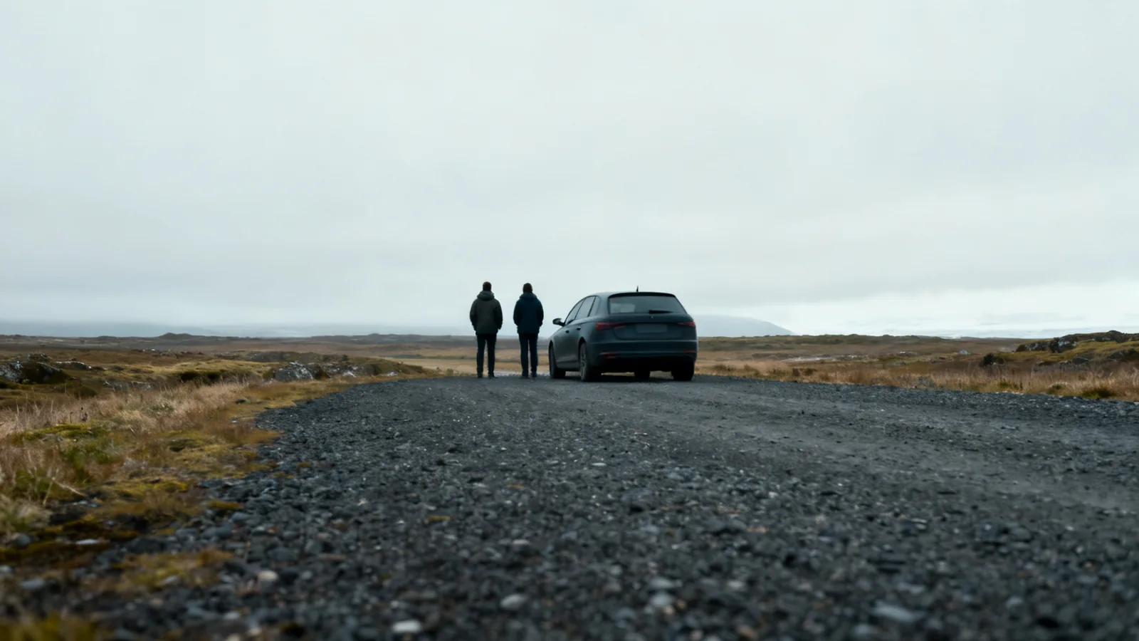 Two distant travellers beside a plain car on an anonymous rural pullout